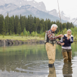 Senior couple standing in an alpine lake with fishing rods