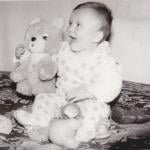 Old cute photo of a baby sitting with toys.