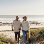 Cheerful elderly couple smiling happily while walking away from the beach after a picnic.