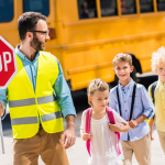 Traffic guard helping young school children cross the road in front of a school bus
