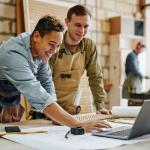 Two carpenters reviewing work on laptop.