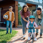 Child learning to ride bicycle with help of her parents.