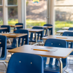 An empty classroom with small blue chairs at desks.