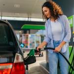 A young woman puts fuel in her car at gas station.