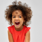Child with curly brown hair and red t-shirt laughing.