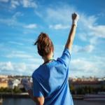 A woman in scrubs holding her hand in the air on a patio facing a city.