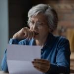 An older woman looking at the sheet of paper in her hand looking distressed and concerned.