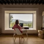 A woman working at a desk looking out on green mountains.