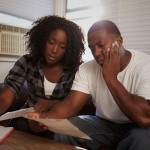 A worried African American couple is looking at papers in front of them. 