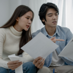 Young, concerned Asian couple looking at the white papers in front of them. 
