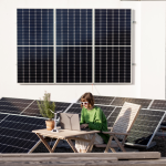 A woman working on a laptop on a rooftop covered in solar panels.