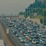 A busy highway with heavy traffic in both directions. Above the highway, there is an electronic sign displaying a message.