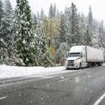 A semi-truck parked on the side of a snowy highway.