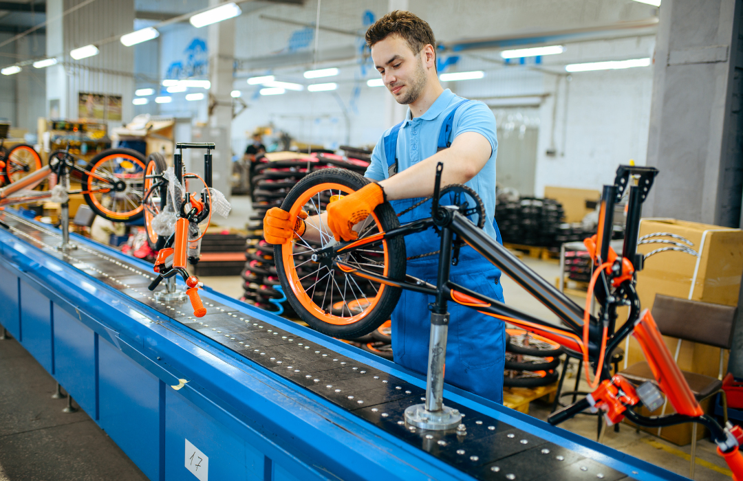 An assembly line worker installing a wheel on an orange bike.