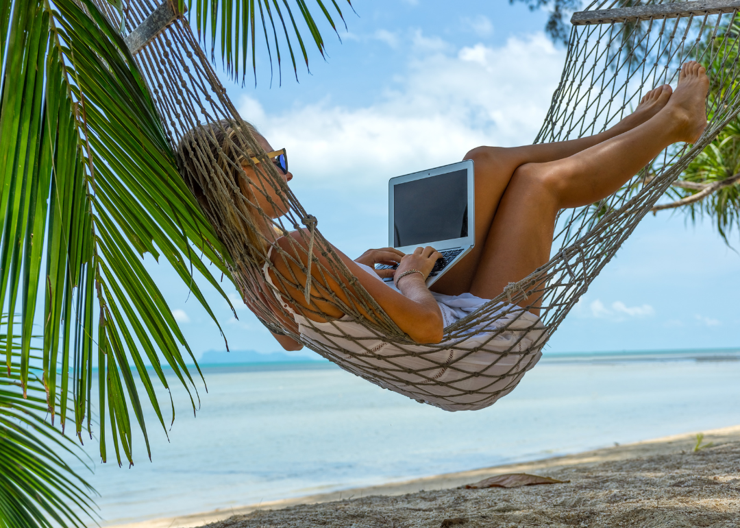 A person doing work in a hammock on a tropical beach