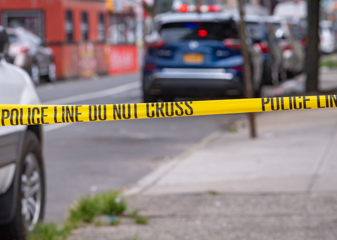 A line of police tape in a city street with cars and buildings in the background.
