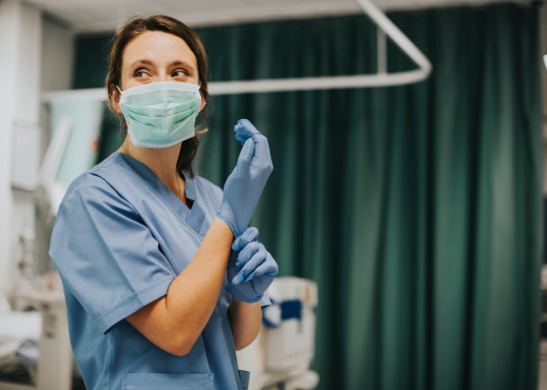 A nurse practioner in a mask putting on their gloves.