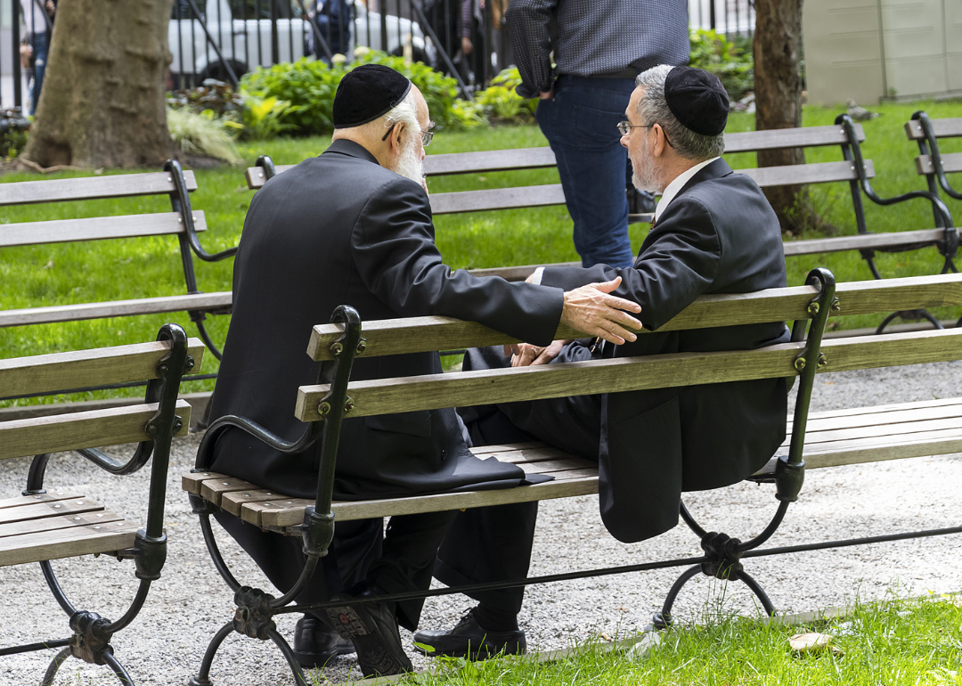 Two Jewish men wearing kippahs talking in a public bench in the financial district.