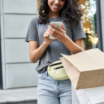 Smiling woman carrying shopping bags and looking at her smartphone.