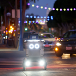 An autonomous robot with the name Esther displayed on its screen making a delivery in the city.