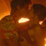 A man and woman kiss passionately in front of a burning ball of color.
