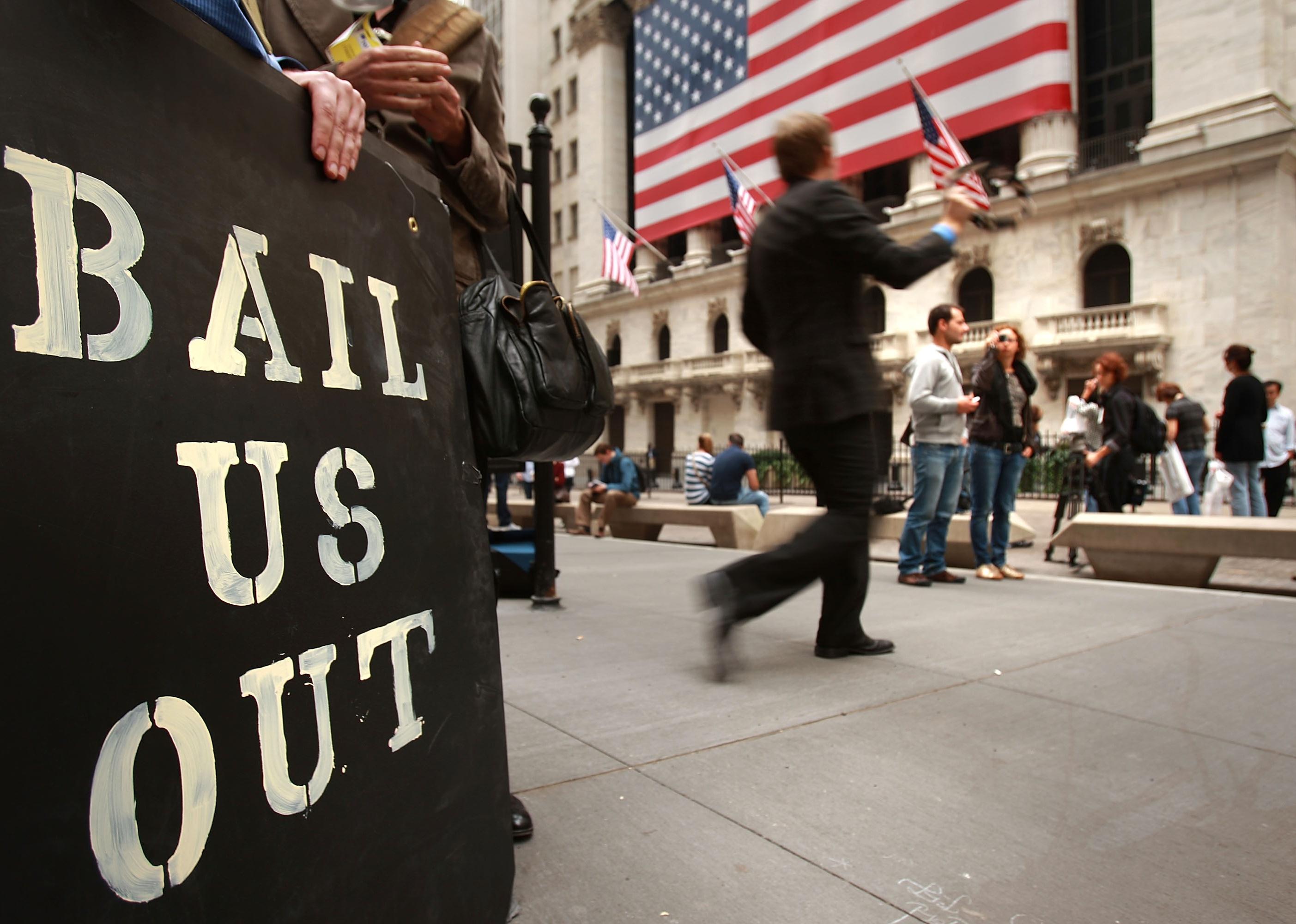 People protest and wave american flags outside of the New York Stock Exchange October 13, 2008 in New York City, holding a black sign reading, "bail us out".