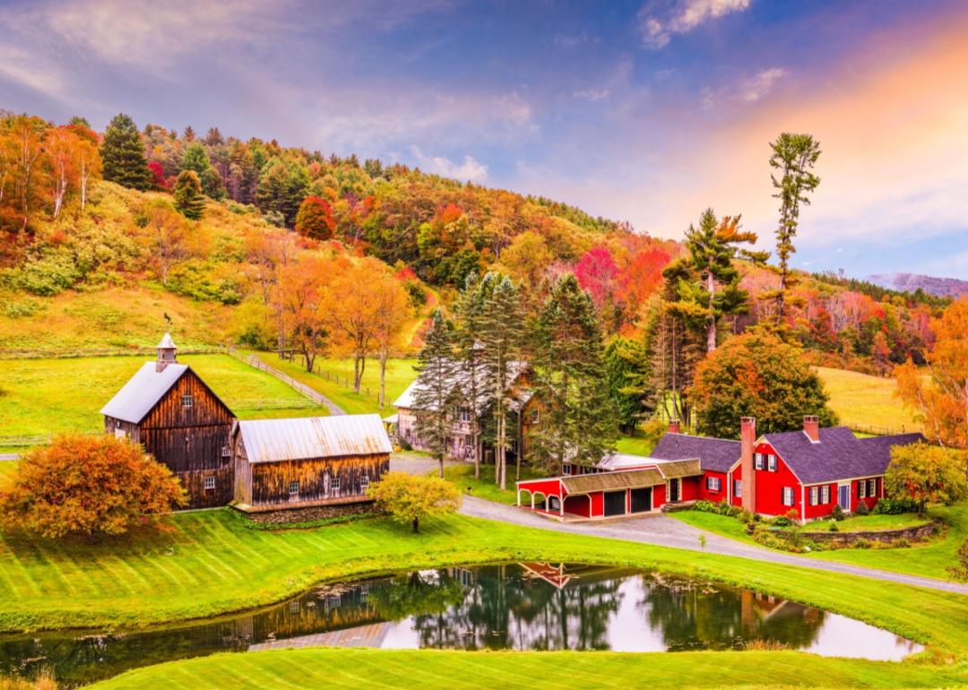 A red farmhouse, wood house and barn in the hills surrounded by Fall trees.