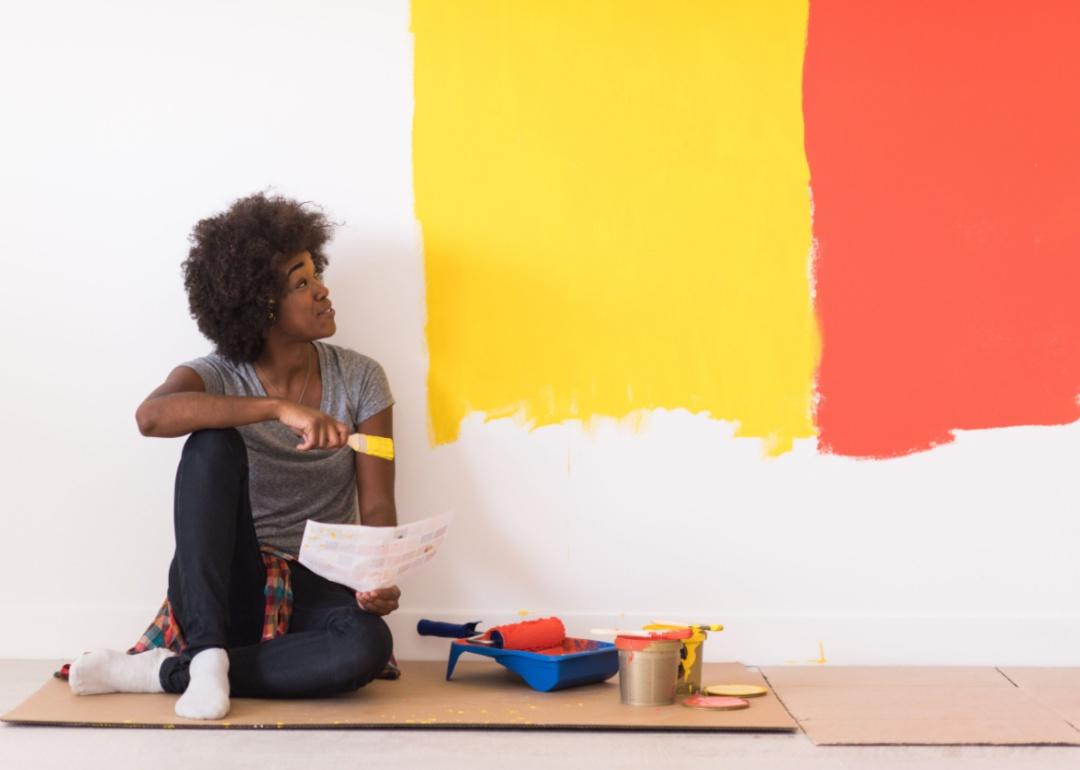 A person testing bright orange and yellow paint colors on a wall.