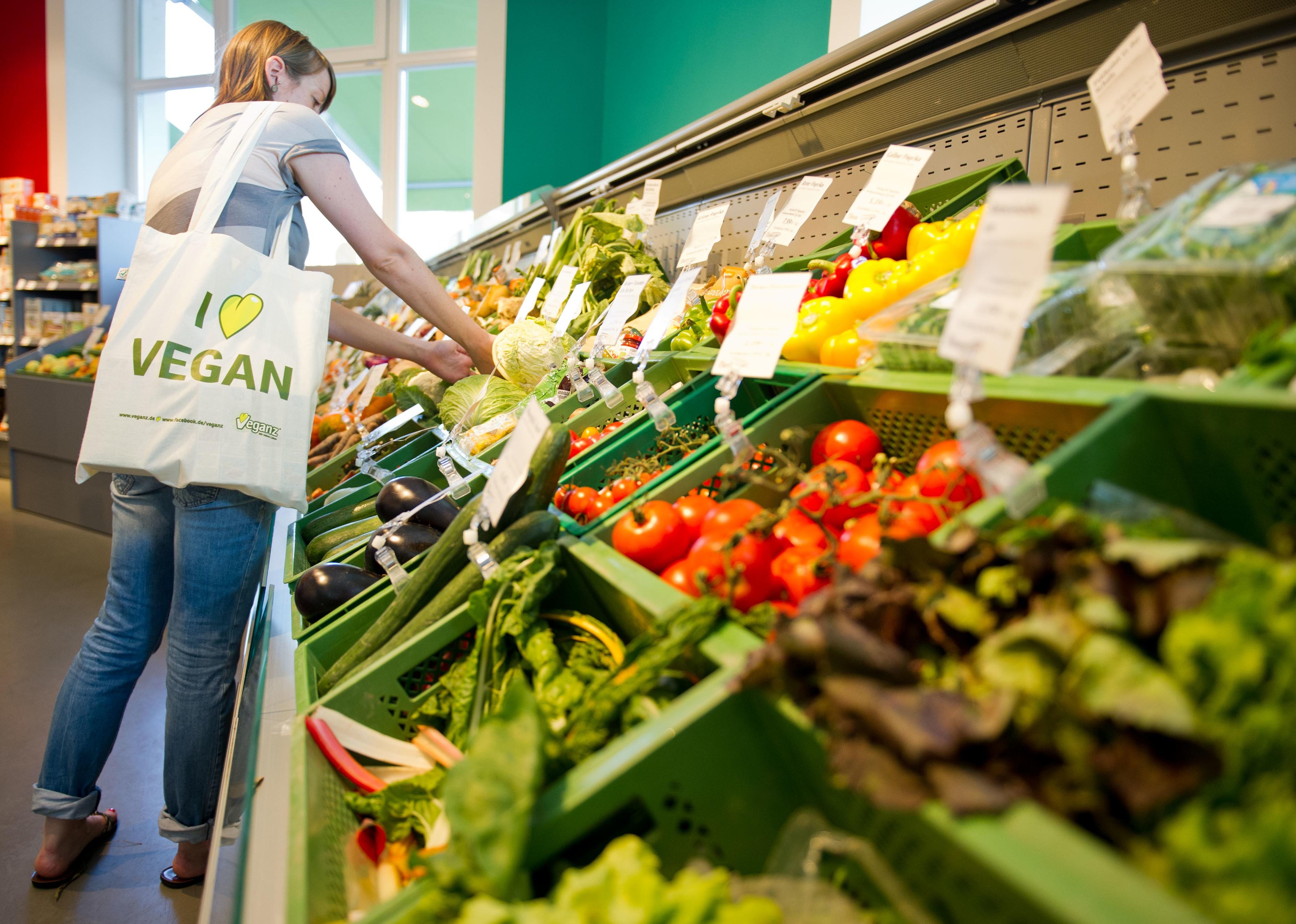 A woman shopping for vegetables with a canvas bag that says I love vegan on it.