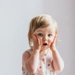 Surprised toddler with hands on her cheeks.