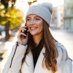 Woman walking outdoors wearing a hat and talking on cell phone.