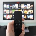 Hand holding a TV remote while watching shows on a streaming service.