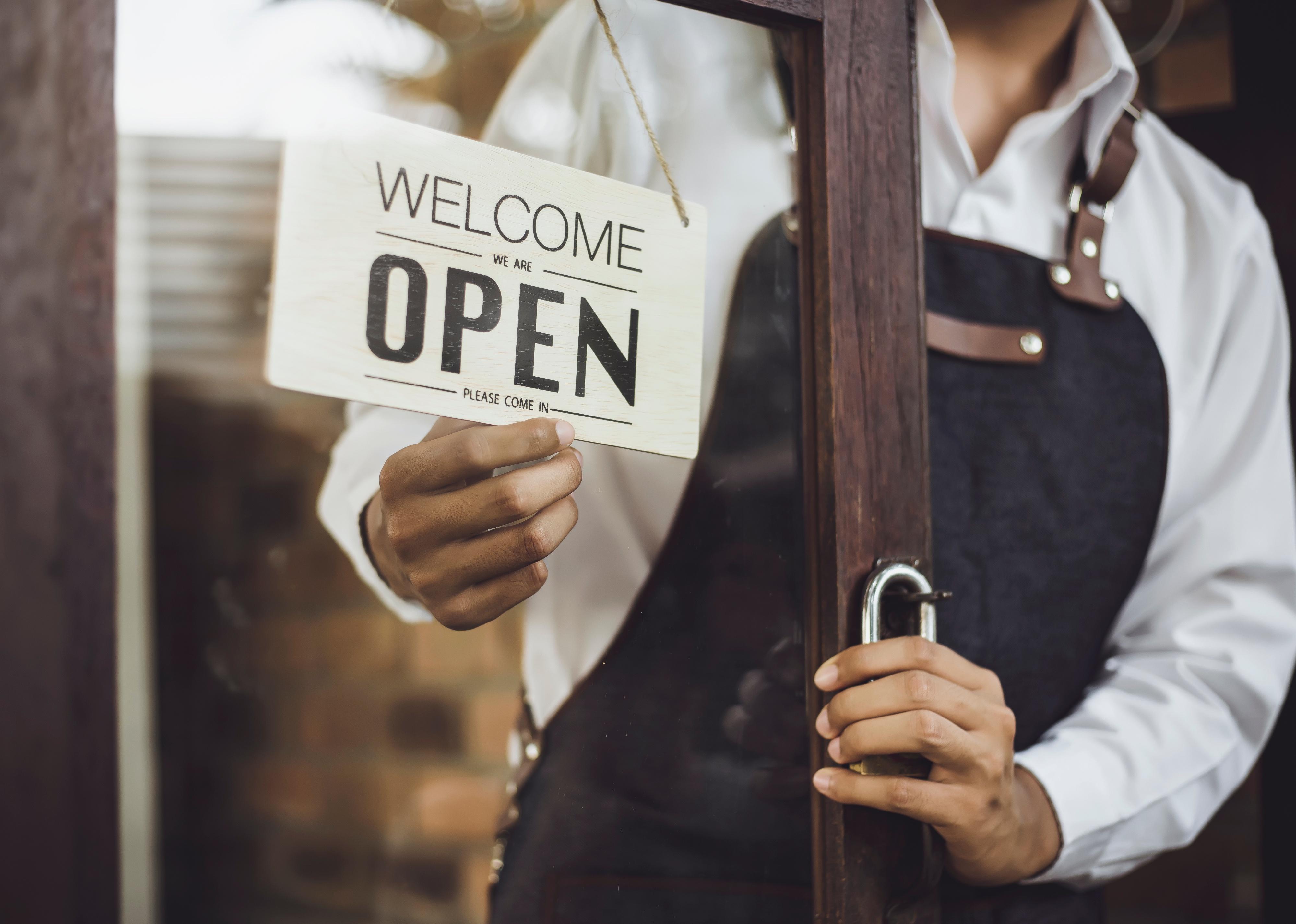 Store owner turning open sign broad through the door glass and ready to service.