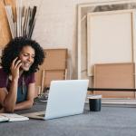 Young female working on a laptop and talking on the phone in a workshop.