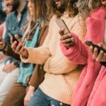 Group of young people using smartphone sitting in a bench.