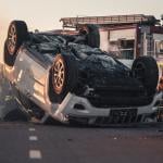 Daytime crash scene with damaged car and first responders.