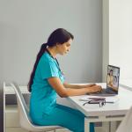 Young female nurse in blue scrubs with a stethoscope gives an online consultation.