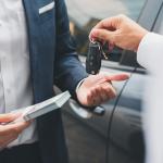 Closeup of a hand giving a car key in exchange for money.