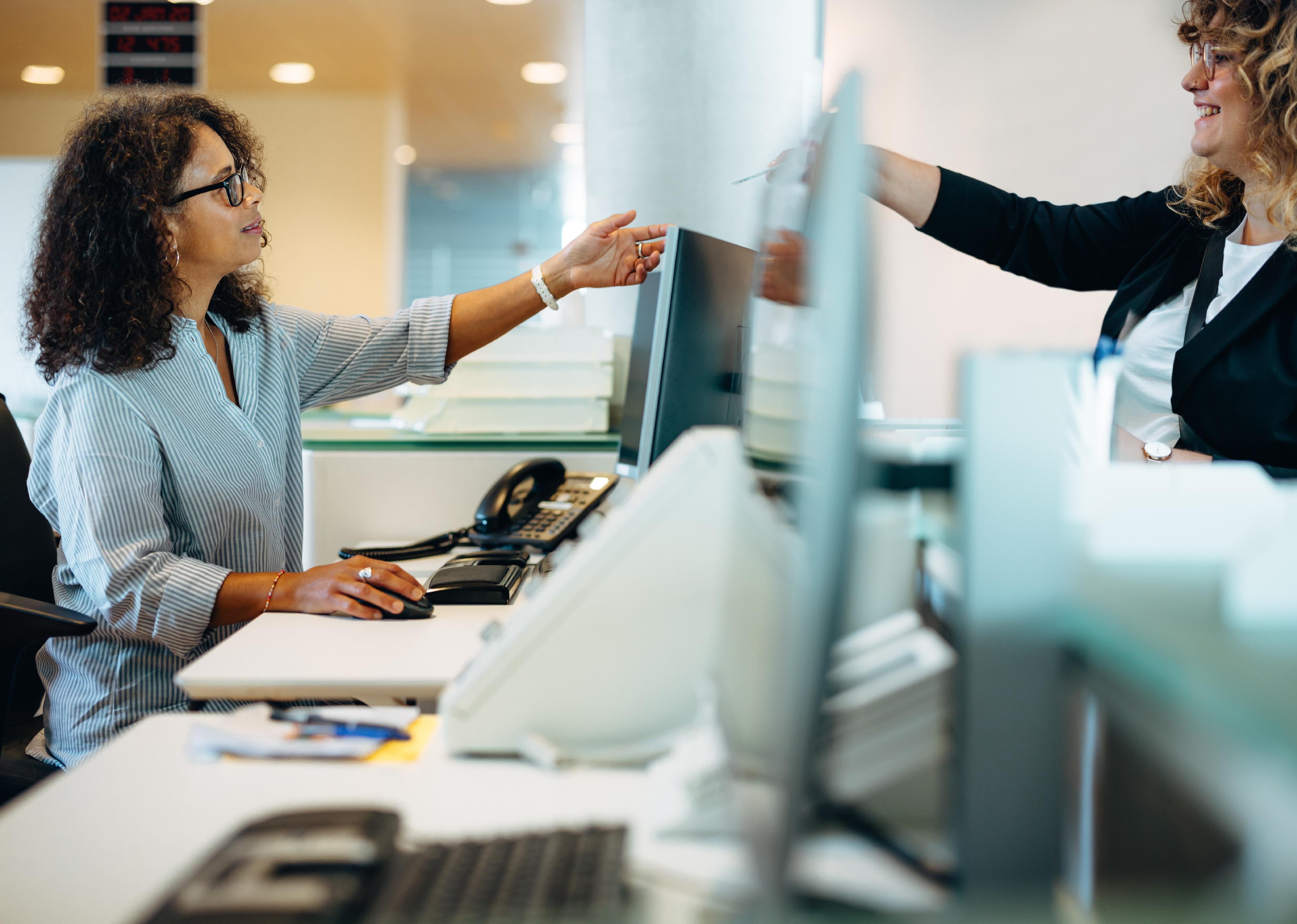 A women hands a credit-card sized card to an employee behind a desk at an office.