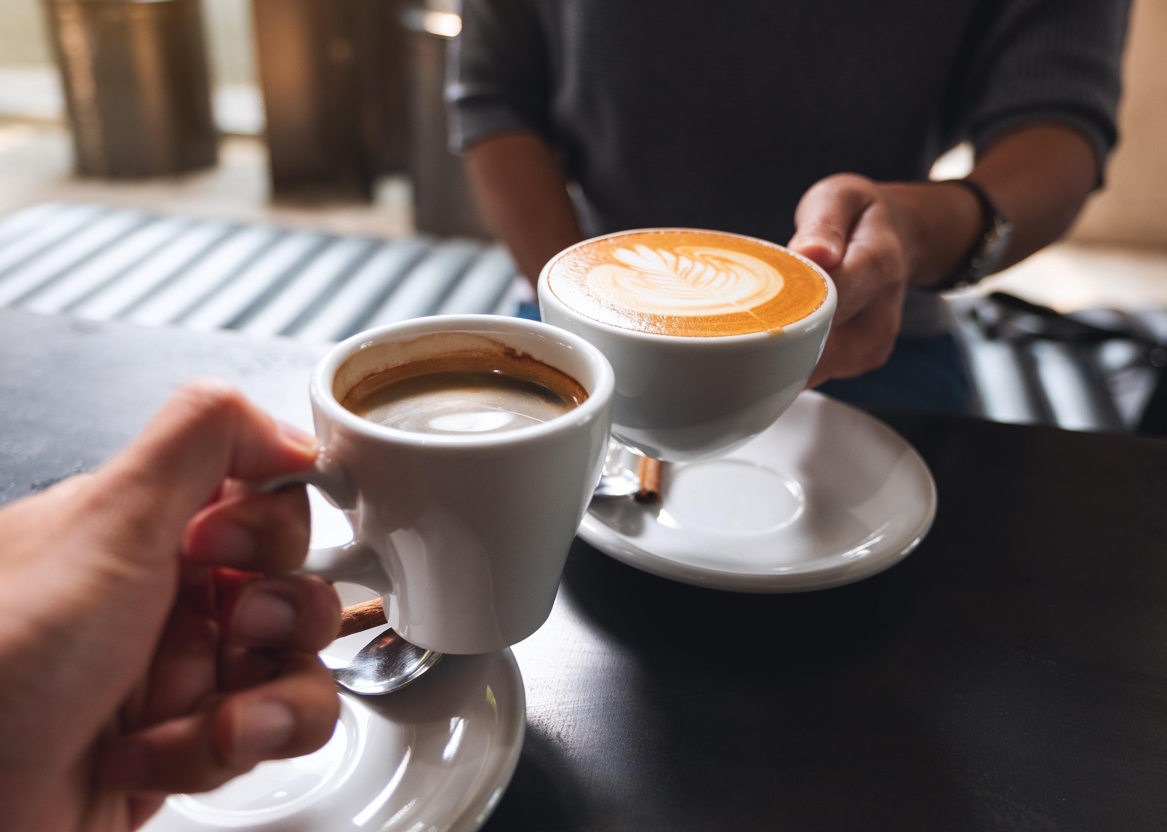 Closeup image of a man and a woman clinking white coffee mugs in cafe