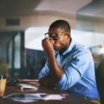 Stressed businessman pinching nose at night in office.