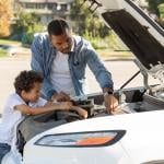 Father and son checking car engine outdoors.