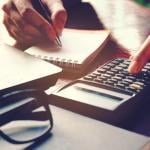 Close up of a person's hand using calculator and writing a note.