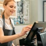 Cheerful cashier using a register for payment.