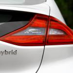 A close up view of the back of a white car with the word hybrid written under the tail light.