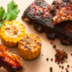 Grilled ribs and grilled corn cobs on a cutting board with a sprig of parsley.