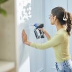 A young woman drilling a hole in her home wall.