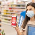 Woman holding up a smart phone with red discount coupon displayed with and drugstore shelves in the background.