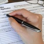 Person filling out paper SBA loan application form by hand.