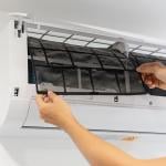 Person pulling out a dirty air conditioner filter from a mini-split unit.